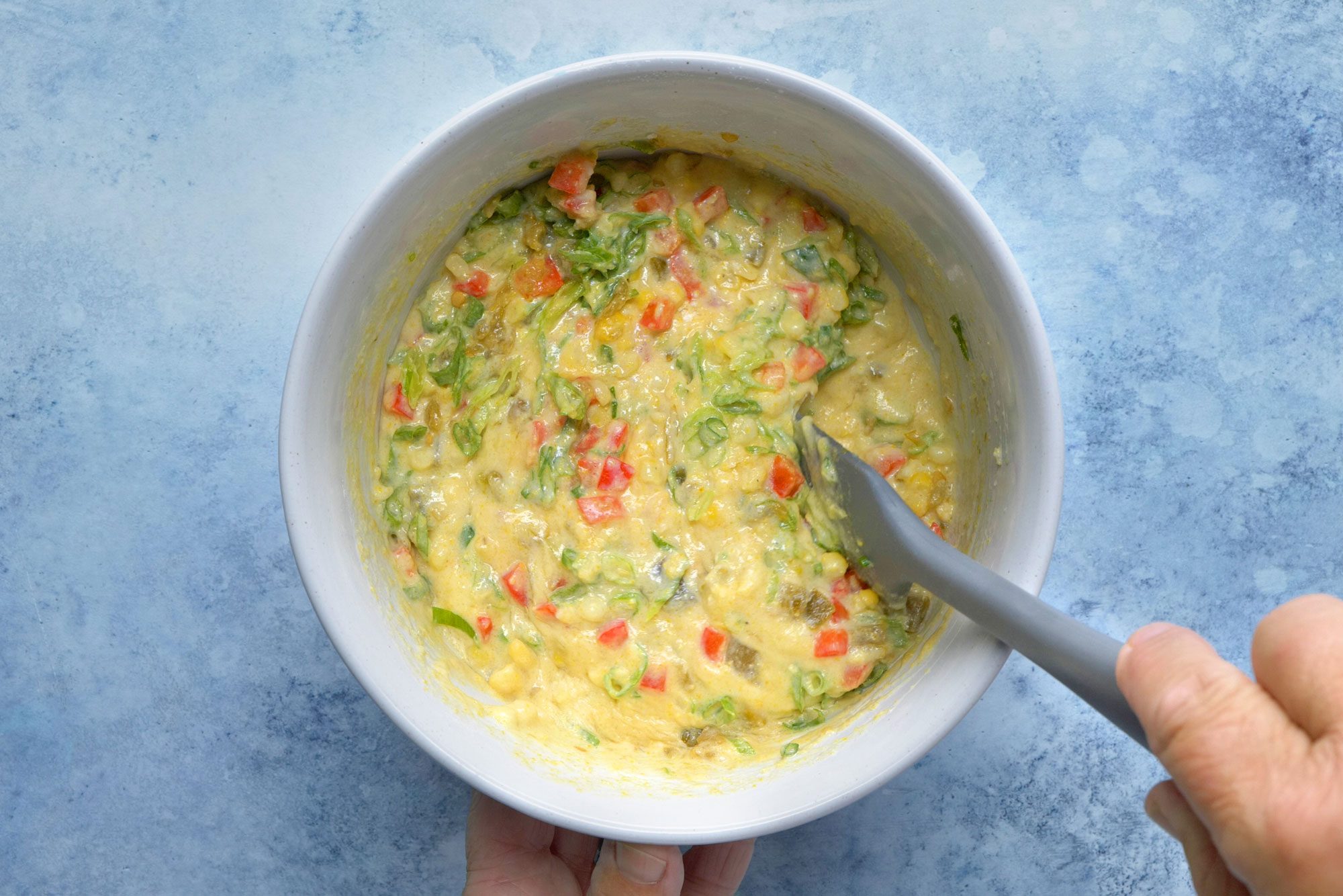 overhead shot; light blue background; added in the corn, green onions, red pepper and green chilies into cake batter;