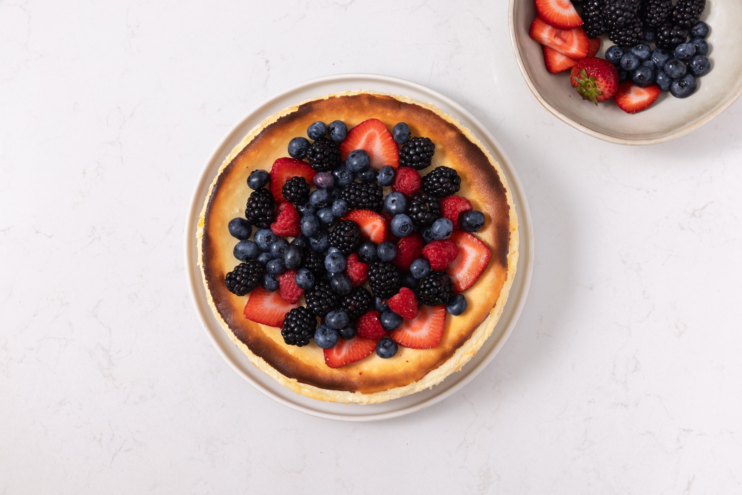 Cheesecake being topped with fresh berries.