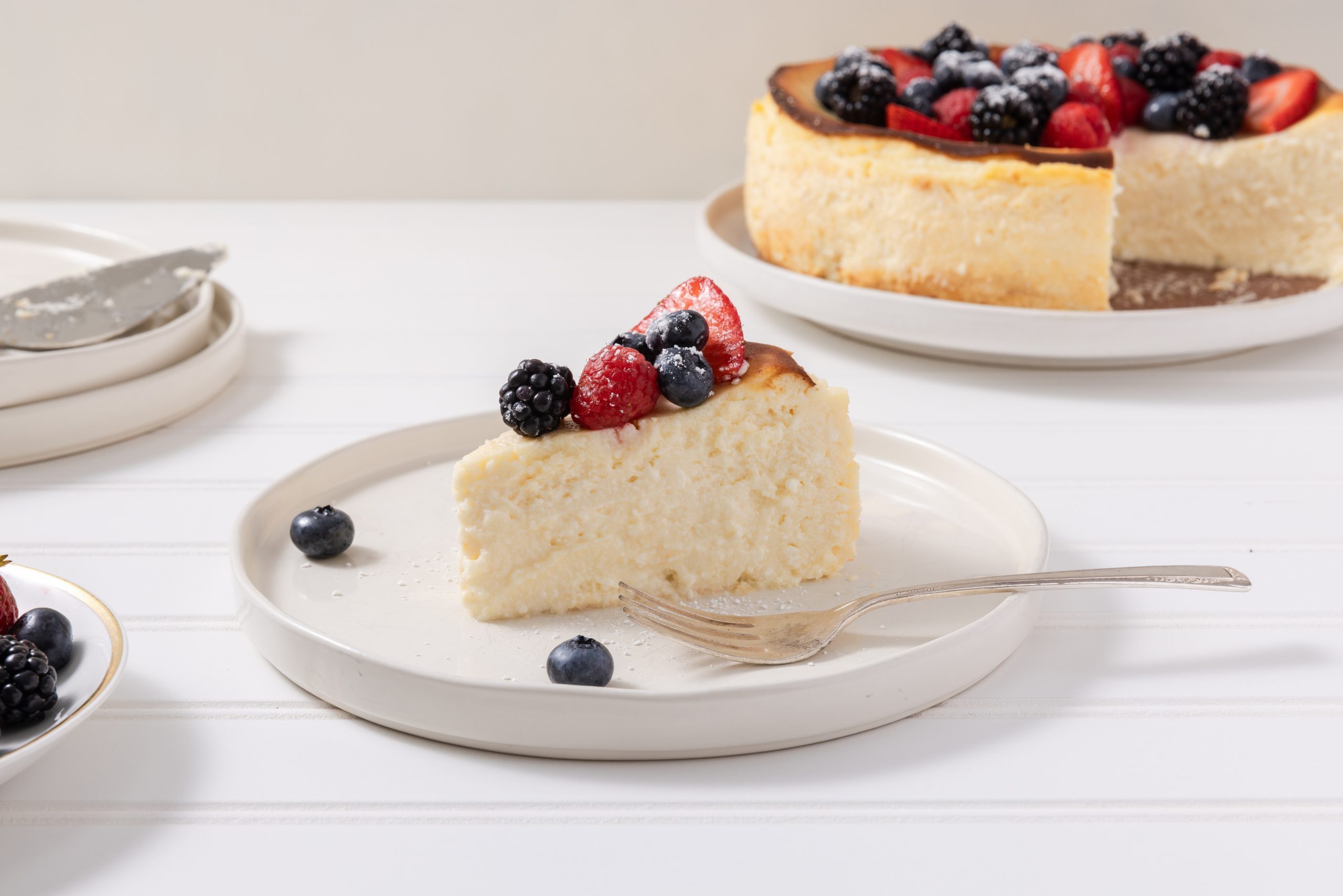 Slice of cheesecake served on plate with full cheesecake in the background.