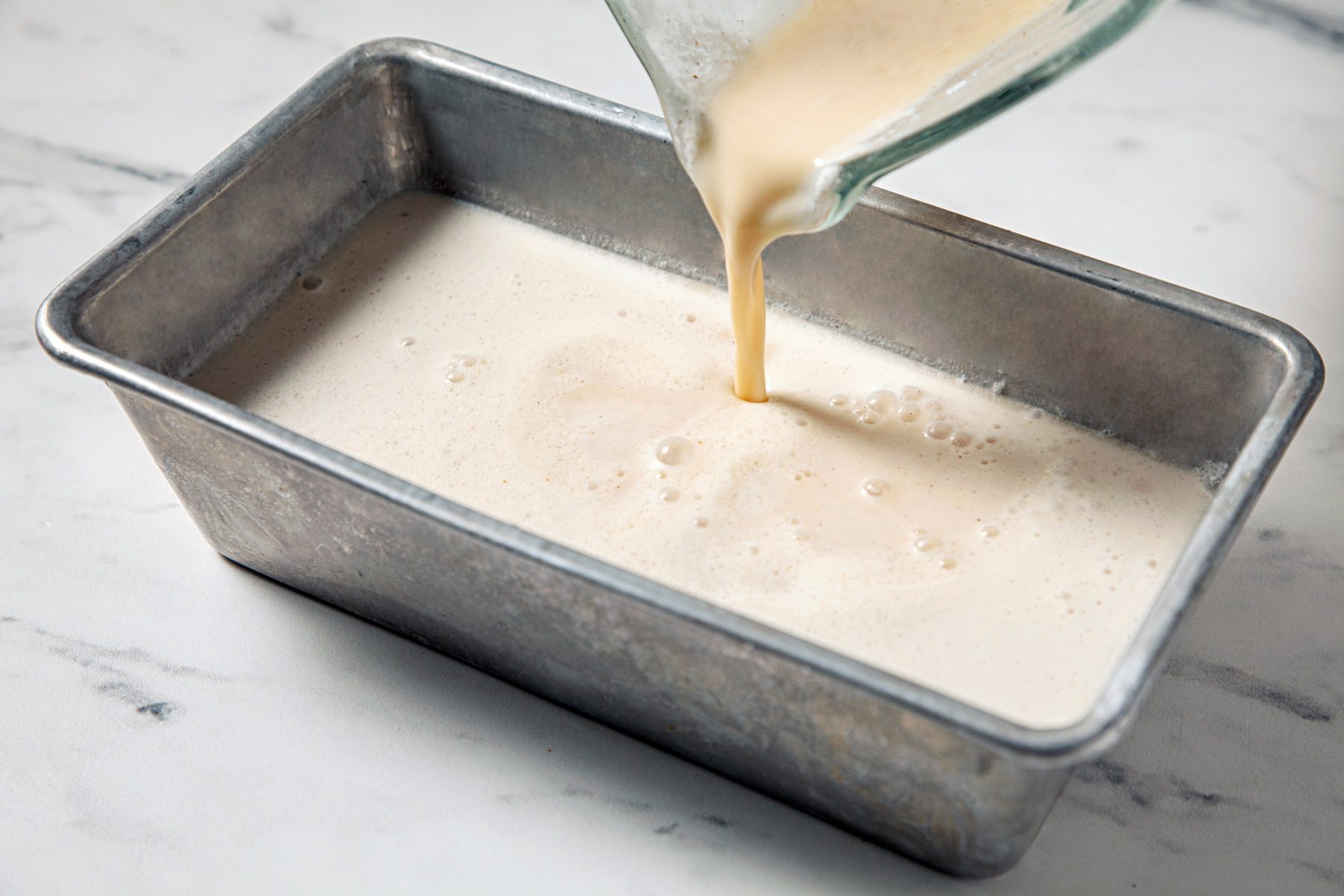 Pouring eggnog ice cream mixture in steel tray to freeze
