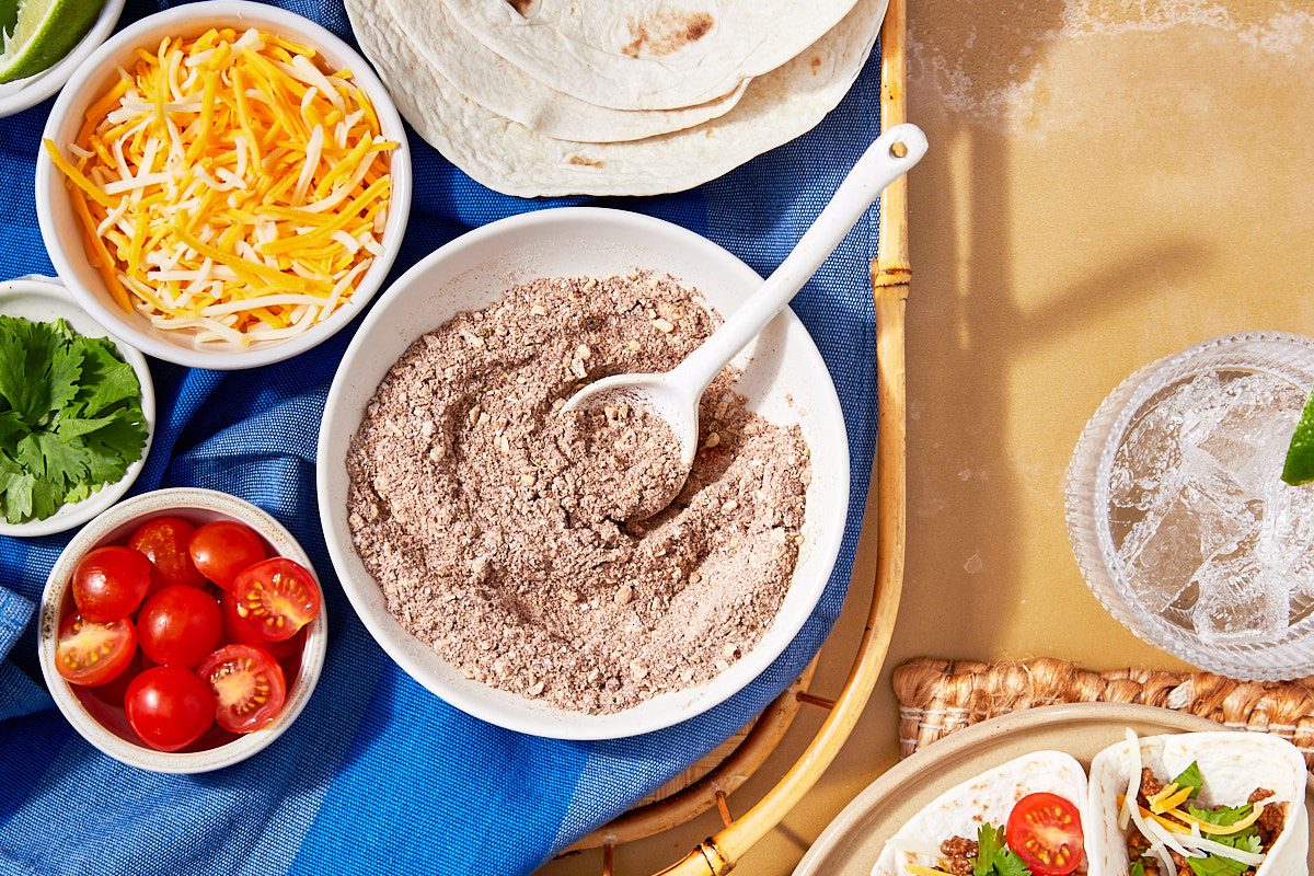 Homemade Taco Seasoning Hero- close up of seasoning in bowl with taco toppings surrounding