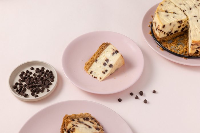 Slice of cheesecake served on plates and full cheesecake next to it.
