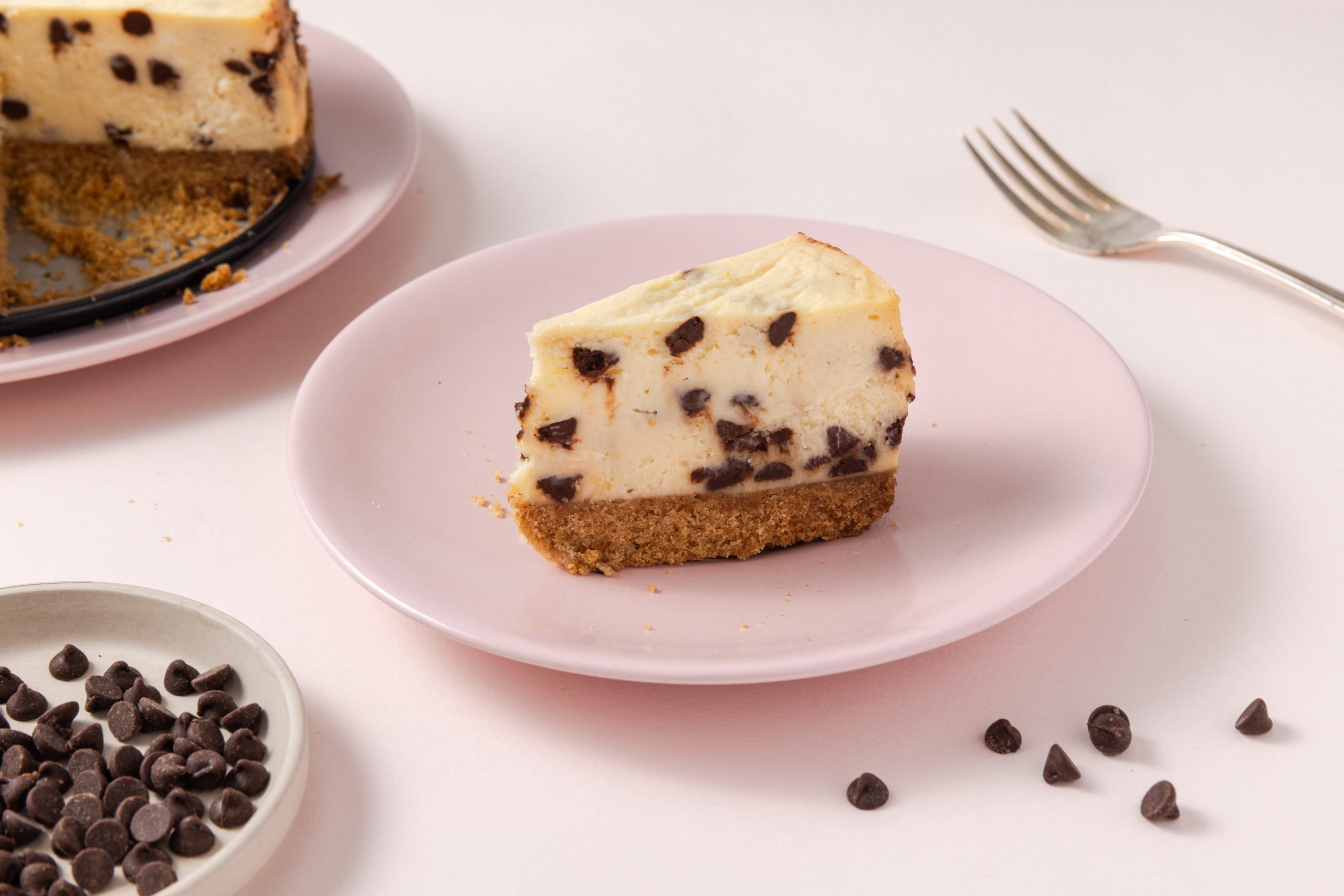 Slice of cheesecake served on plates and full cheesecake next to it.