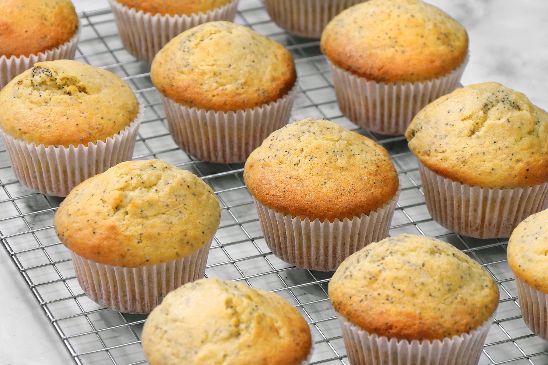 Golden brown muffins in white paper liners are cooling on a metal wire rack. 
