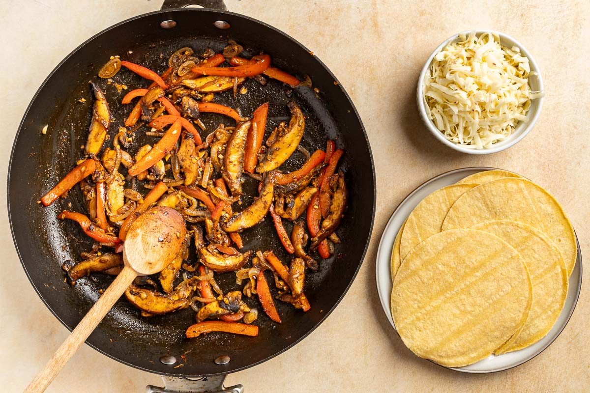 Taste of Home Mushroom Tacos recipe photo of the finished sauteed veggies with warm corn tortillas and cheese for topping.