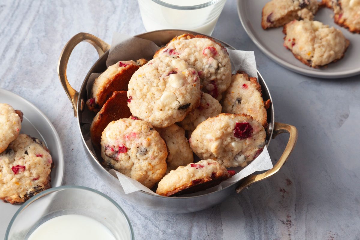 Full yield of Taste of Home Oatmeal Cranberry Cookies in a silver metal bowl with handles, milk glasses