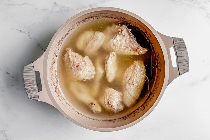 Poached chicken in a Dutch oven set on a marble surface for Taste of Home okra gumbo.