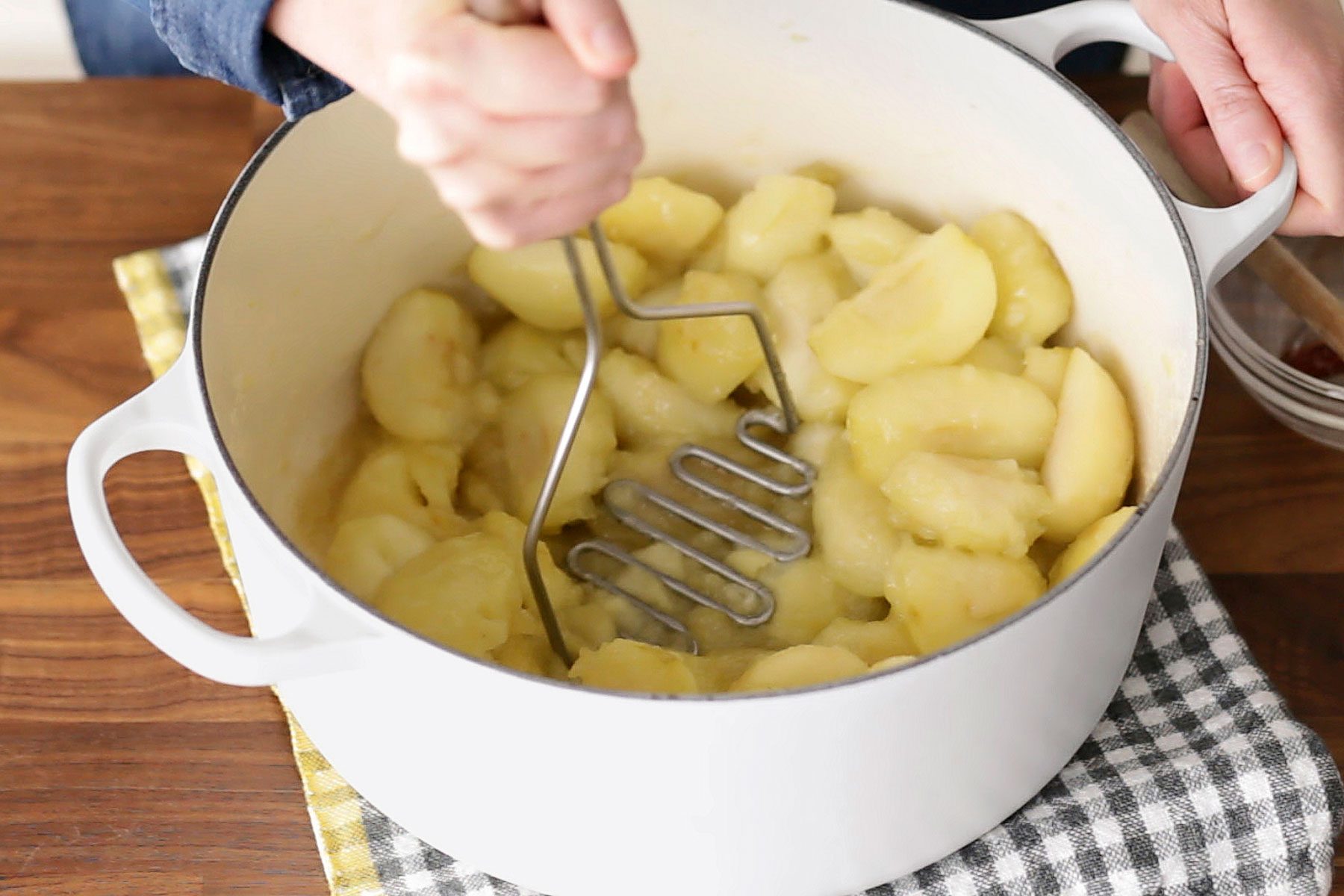 Person mashing cooked apples in a dutch oven
