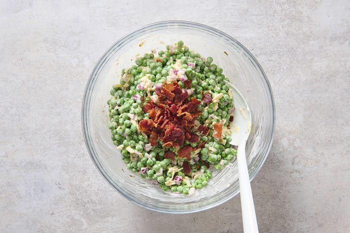Stirring crumbled bacon into the chilled pea salad
