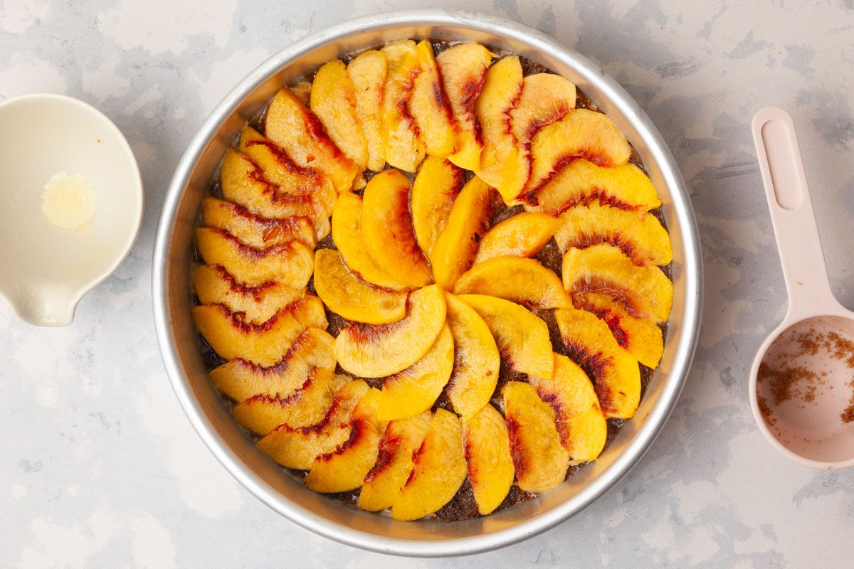 Step 1 of Taste of Home Peach Upside-Down Cake is to Melt 1/4 cup of butter, then pour it into an ungreased 9-inch round baking pan. Sprinkle the butter with brown sugar, then arrange the peach slices in a single layer over the sugar.