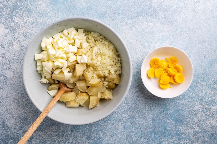 Taste of Home Potato Salad Recipe photo of potatoes and other ingredients in a mixing bowl with with a bowl of hard boiled egg yokes on the side.