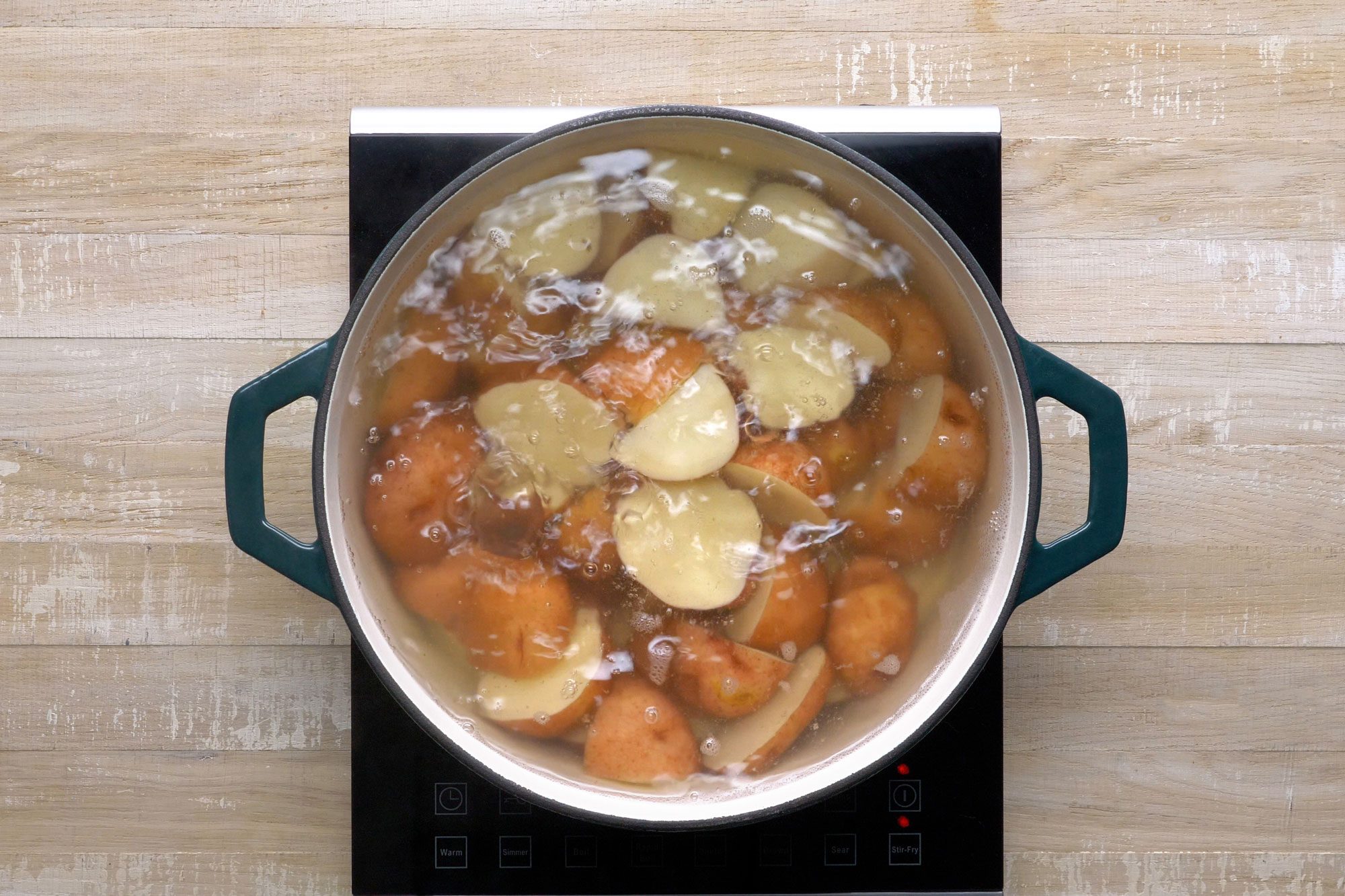 overhead shot; wooden background; boiling potatoes; Placed in a large kettle; covered with water;