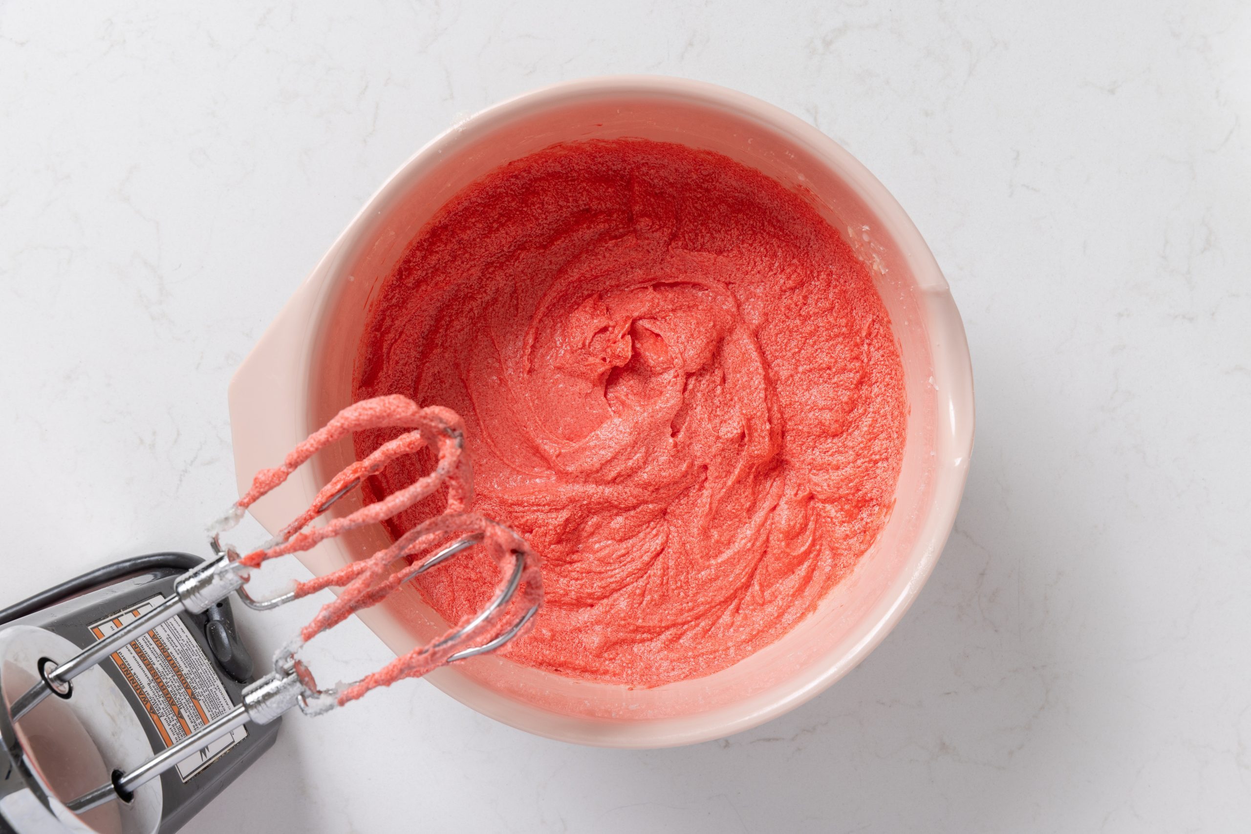 Eggs, vanilla extract, white vinegar and food coloring being added to the sugar and butter mix.