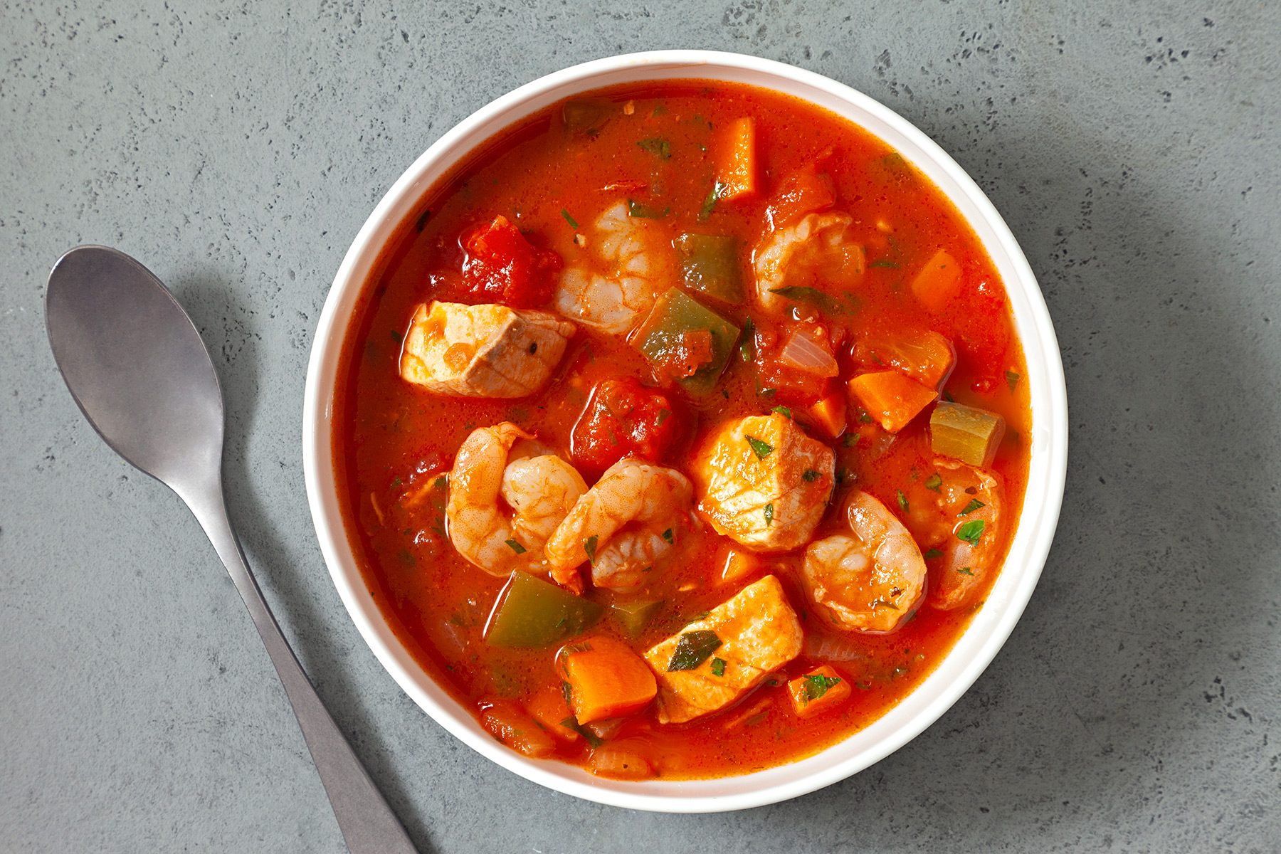 overhead shot; grey background; Seafood Soup served in a white bowl with silver spoon;