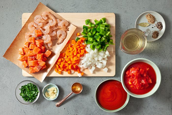 overhead shot; grey background; Seafood Soup ingredients placed on a wooden board and background;