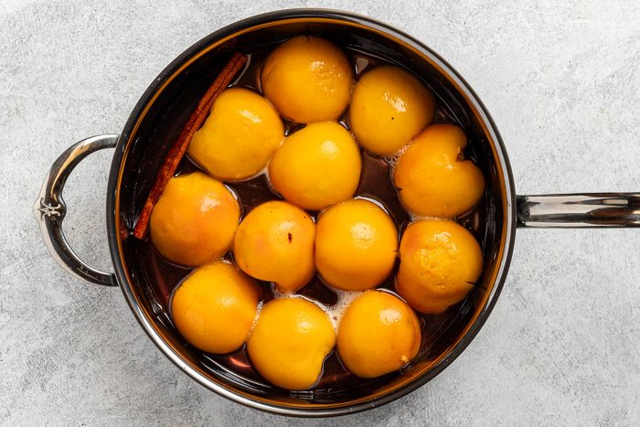 Taste of Home Spiced Peaches recipe photo of the peeled peaches poached in a saucepan.