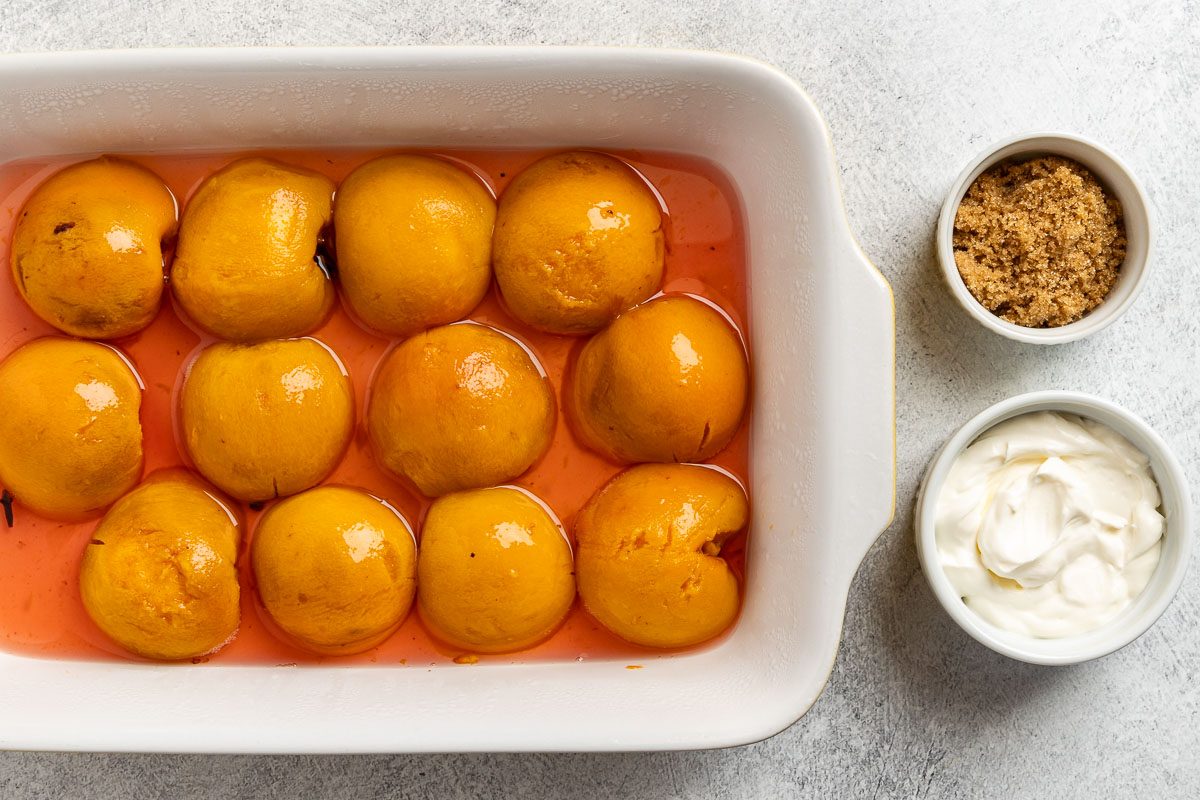 Taste of Home Spiced Peaches recipe photo of the poached peaches chilled in a dish with a side of sour cream and brown sugar to garnish.