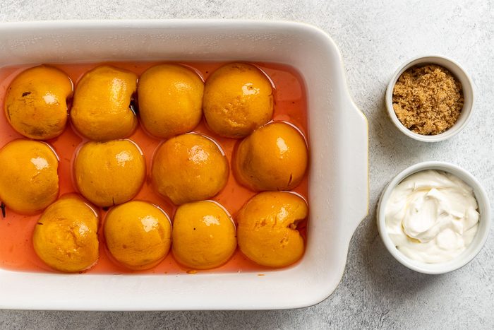 Taste of Home Spiced Peaches recipe photo of the poached peaches chilled in a dish with a side of sour cream and brown sugar to garnish.