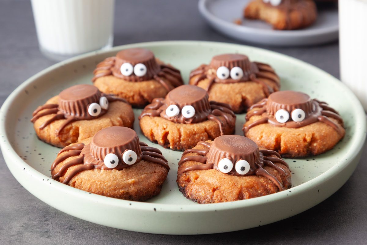 Full yield of Taste of Home Spider Cookies on a green plate, glasses of milk in background