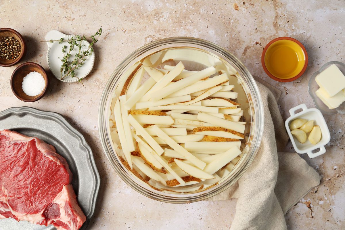 A how to look into Taste of Home's homemade Steak Frites. Sliced potatoes being soaked in cold water in a bowl.