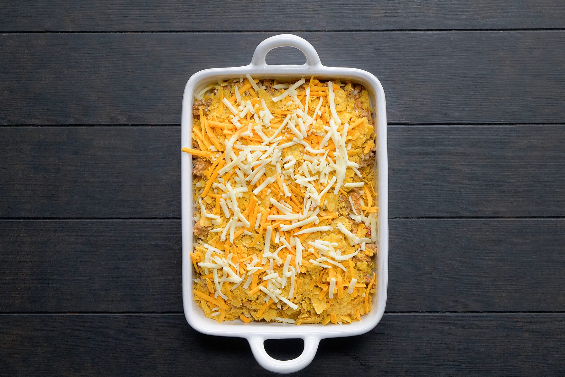 overhead shot; black background; In an baking dish, layered half of the meat mixture with chips and cheeses.