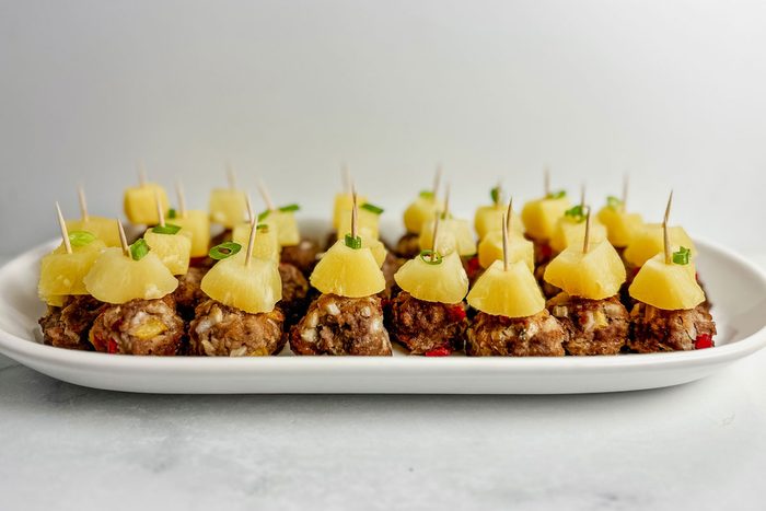 Taste of Home teriyaki meatballs topped with pineapple chunks in a white ceramic tray on a marble surface.