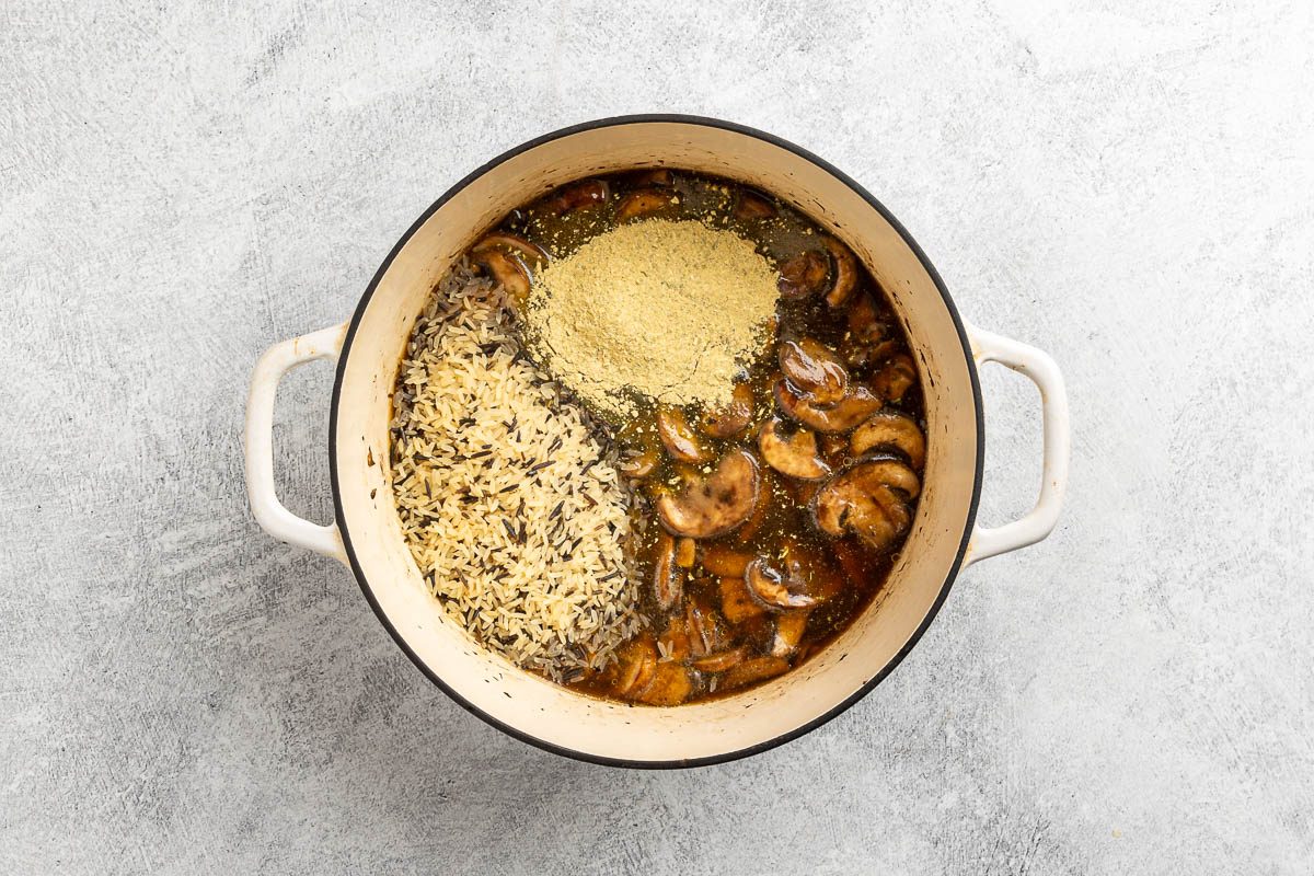 Taste of Home Wild Rice and Mushroom Soup recipe photo of the rice, seasoning packets, broth, and water added to the dutch oven.