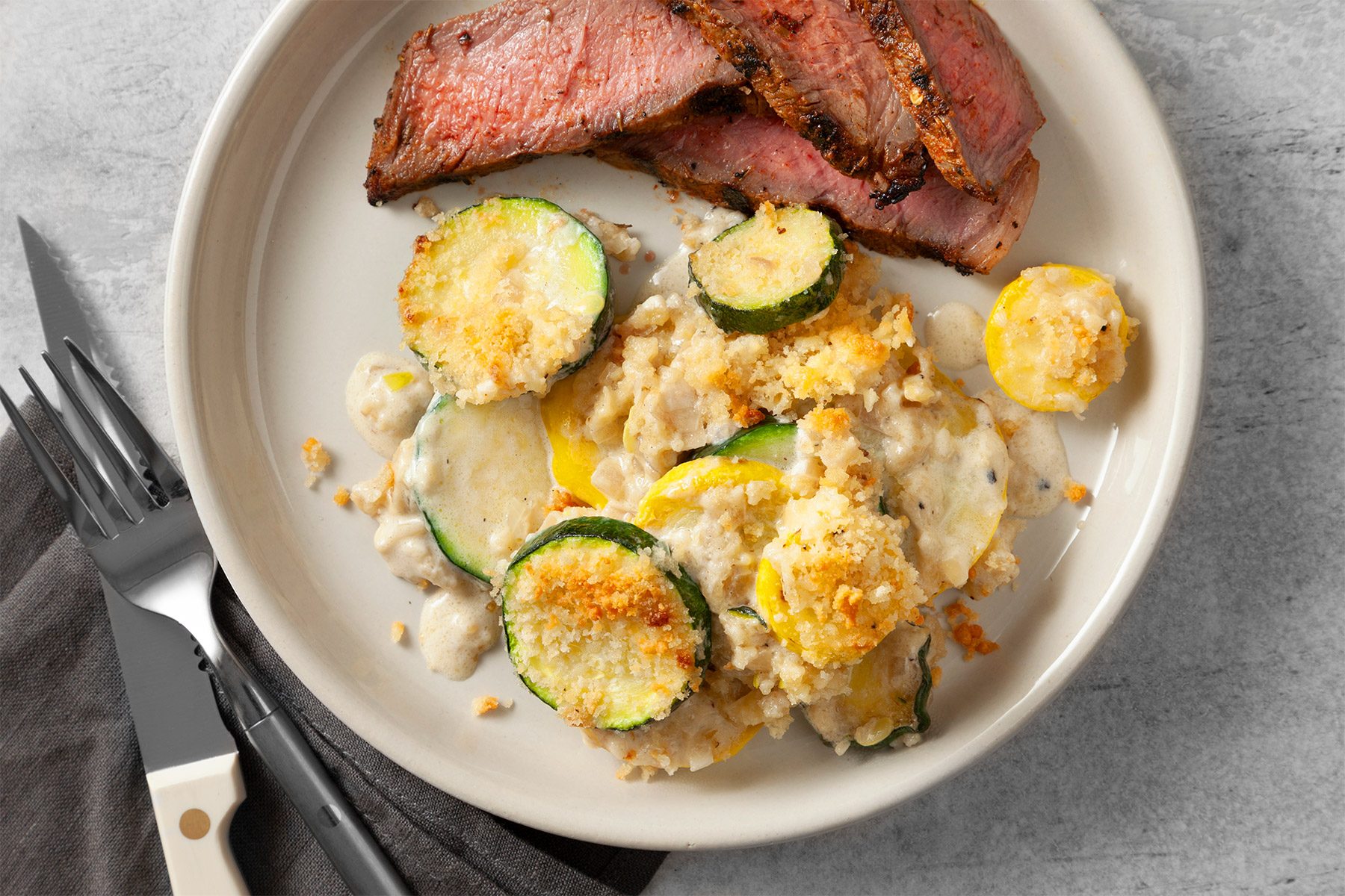 wide shot of yellow squash and zuchhine gratin served with steaks