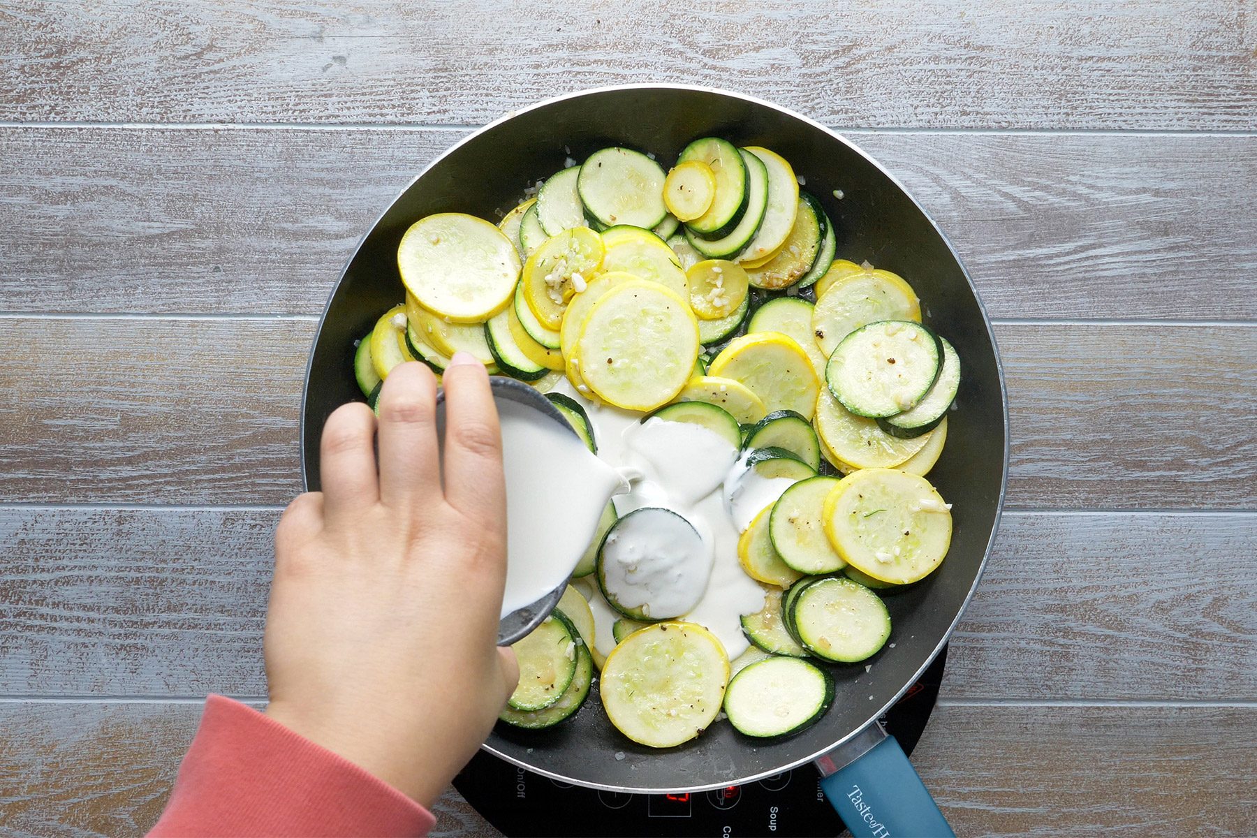 overhead shot of cream added in the cooked zucchini, yellow squash in a large skillet