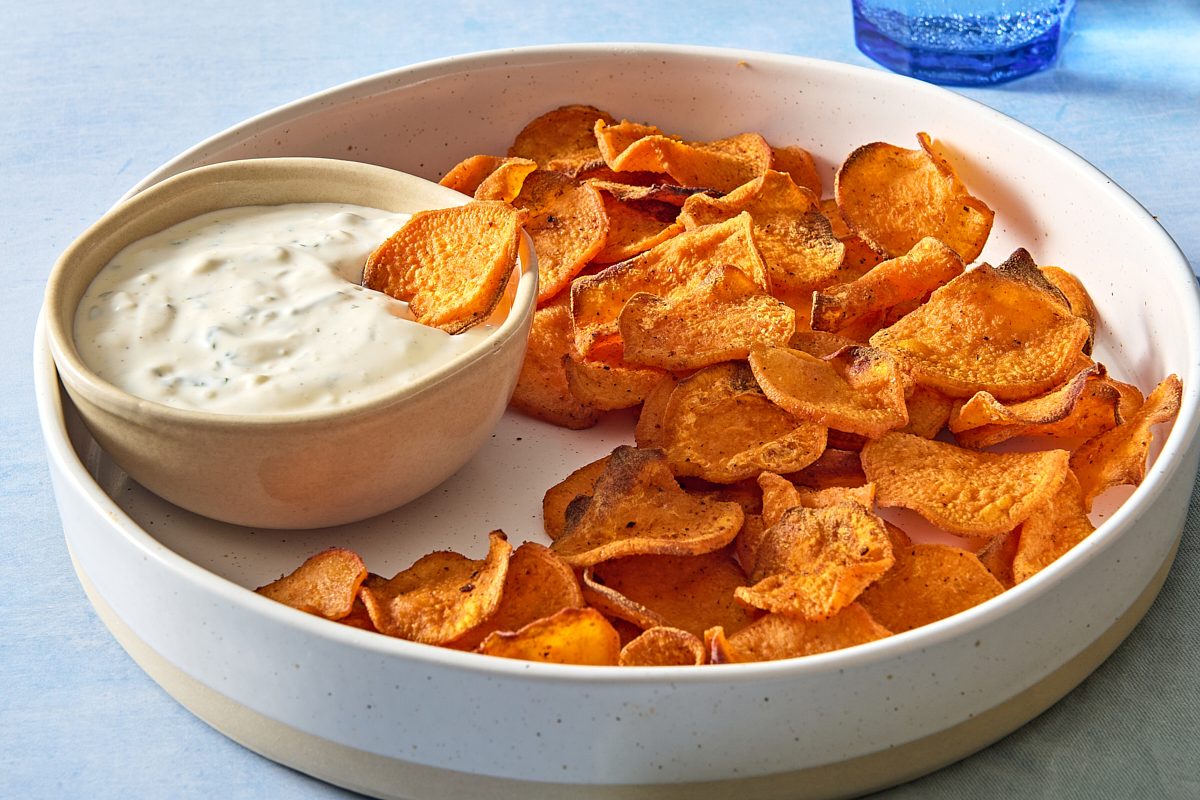Closeup shot of a platter of air fryer sweet potato chips with one being dipped into the dipping sauce