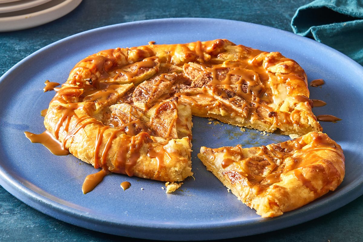 Closeup shot of apple crostata drizzled with caramel and with a slice removed to show the filling