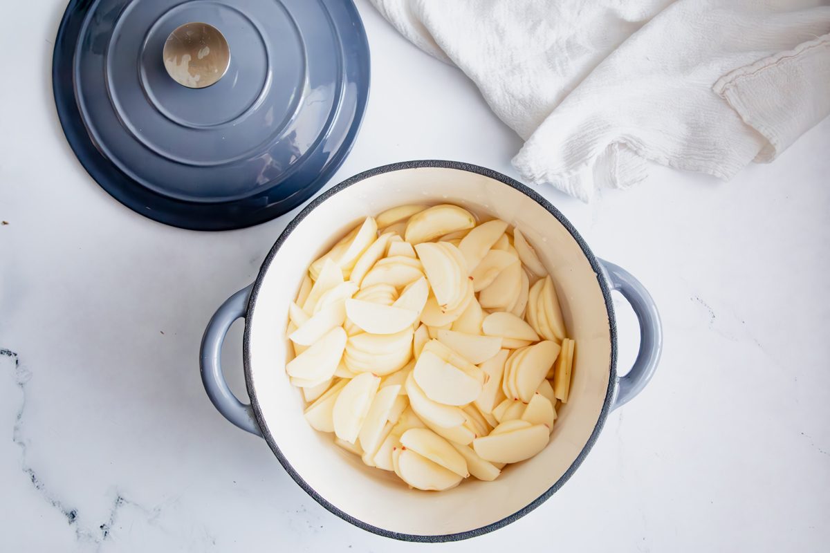 Overhead shot for Taste of Home Apple Jam, apples peeled and in crockpot on a marble surface.