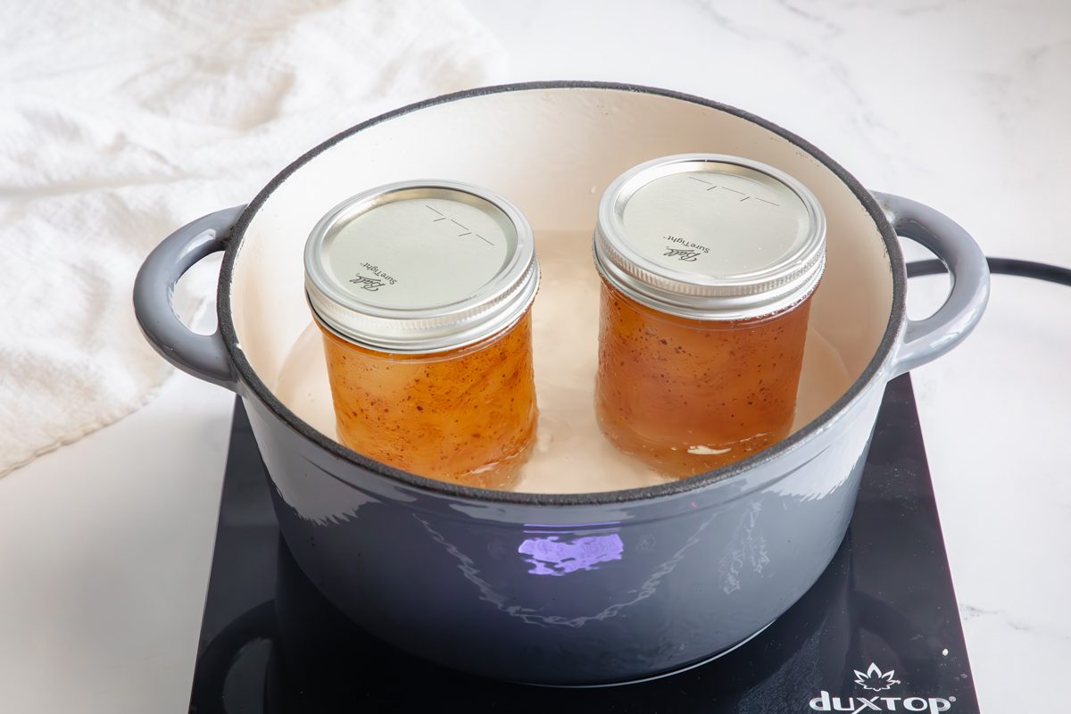 Apple jam inside of mason jars in boiling water in a crockpot on an induction cooktop for Taste of Home.