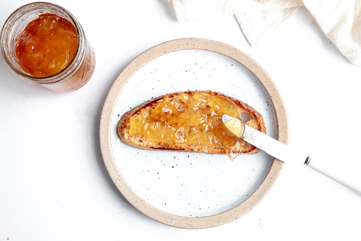 Spreading Taste of Home Apple Jam on toast while on a plate on a marble surface.