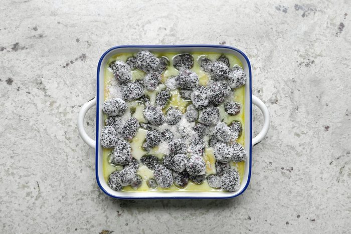 Top view of a white baking dish with blue trim filled with what appears to be a creamy baked dish, possibly featuring coated or dusted small dark objects, on a textured, light-colored surface.