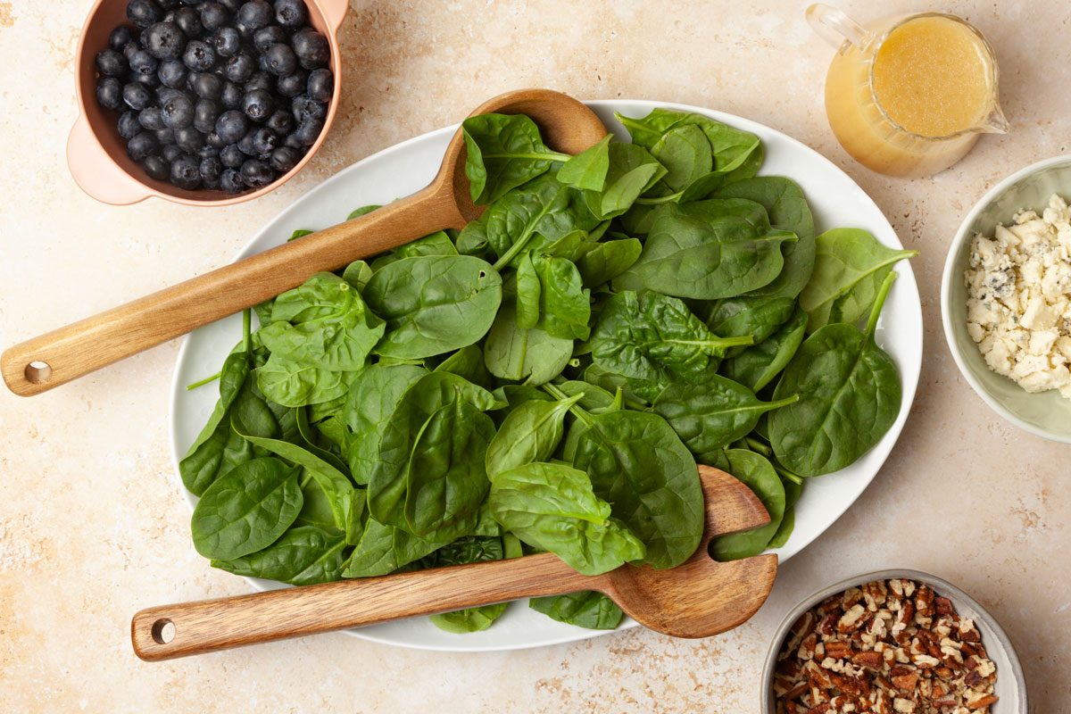 Step 2 of Taste of Home Blueberry Salad is to place the spinach, blueberries, blue cheese and pecans. Drizzle the dressing over the salad, and toss to combine.
