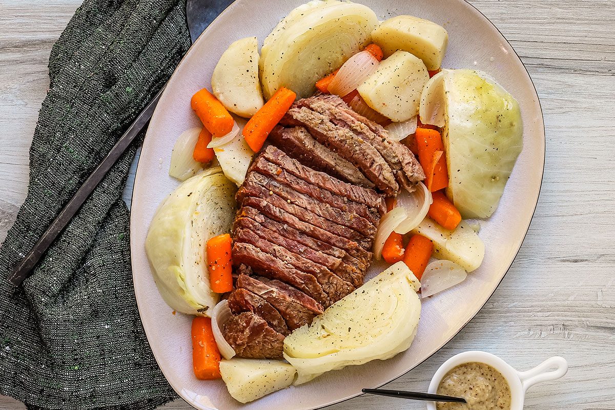 A corned beef boiled dinner with potatoes, carrots, and cabbage, arranged on a large platter.