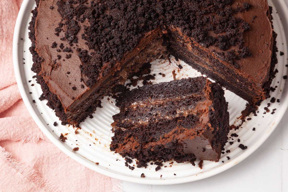 Full field of Taste of home Brooklyn Blackout Cake ona. white plate, white tile surface, black stone background; pink linen