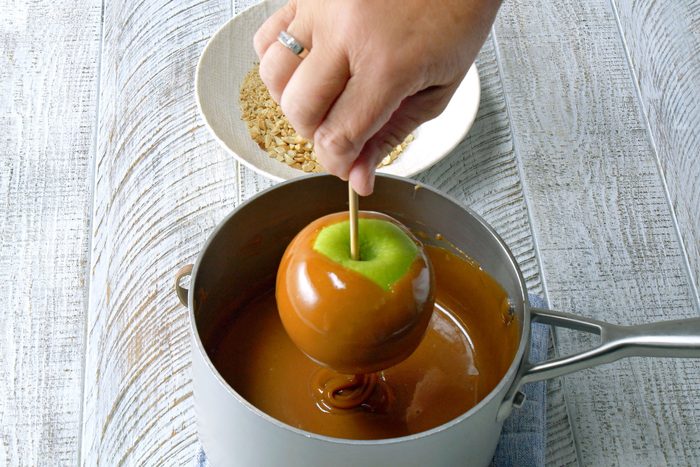 Insert wooden sticks into apples and Dip each apple into hot caramel mixture