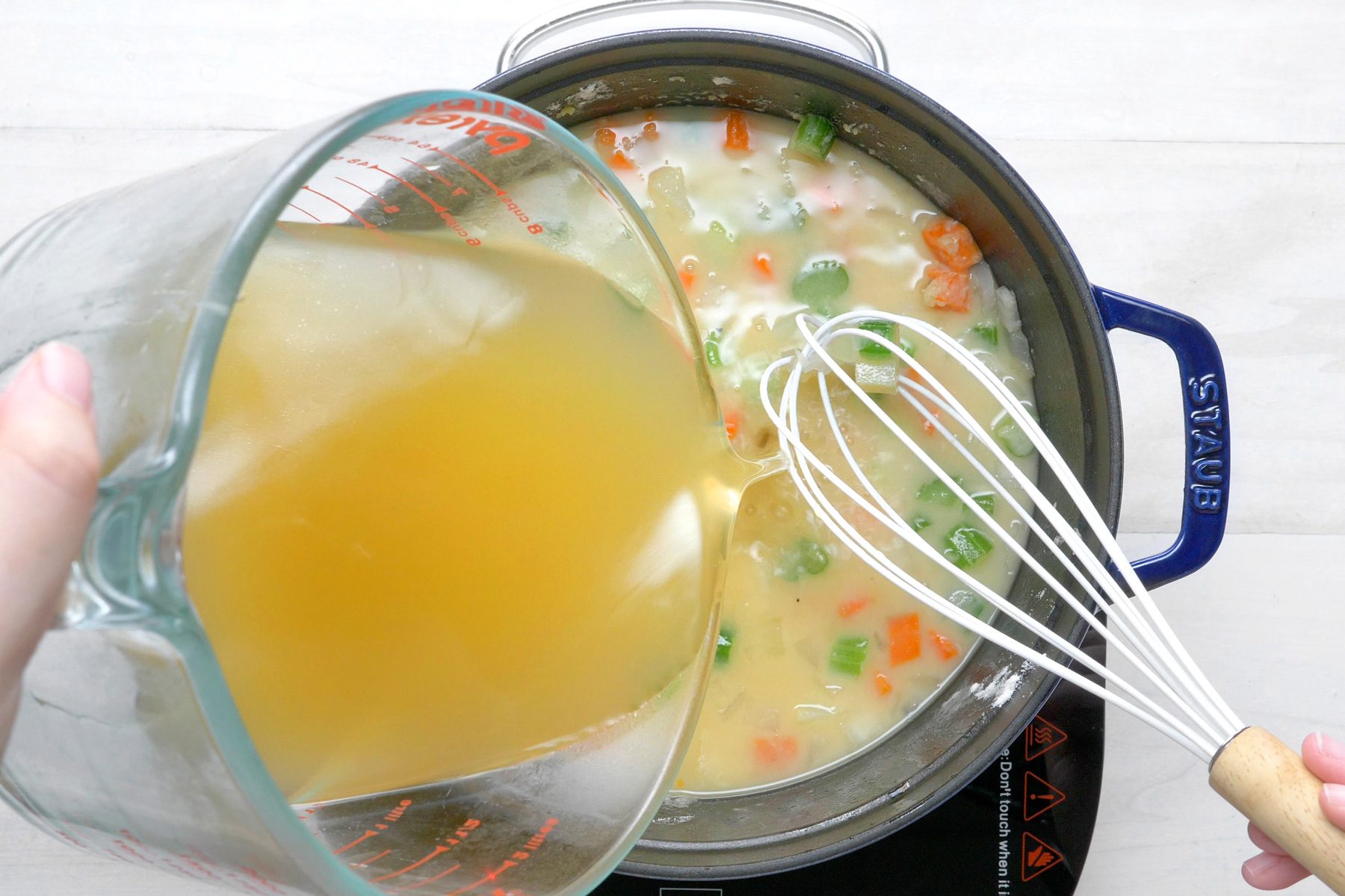 overhead shot; white wooden background; adding broth into saucepan