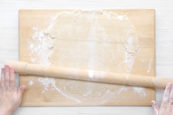 overhead shot; white wooden background; flattening the dough with roller over wooden board