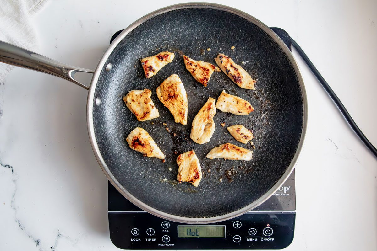Overhead shot for Taste of Home Chicken Gyros, chicken cooking in a skillet on an induction cooktop on a marble surface.