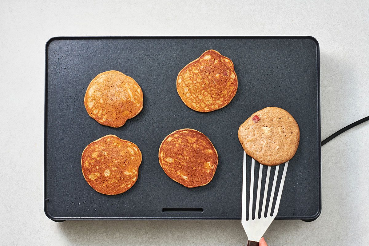 Cooked pancakes on the griddle with one being flipped