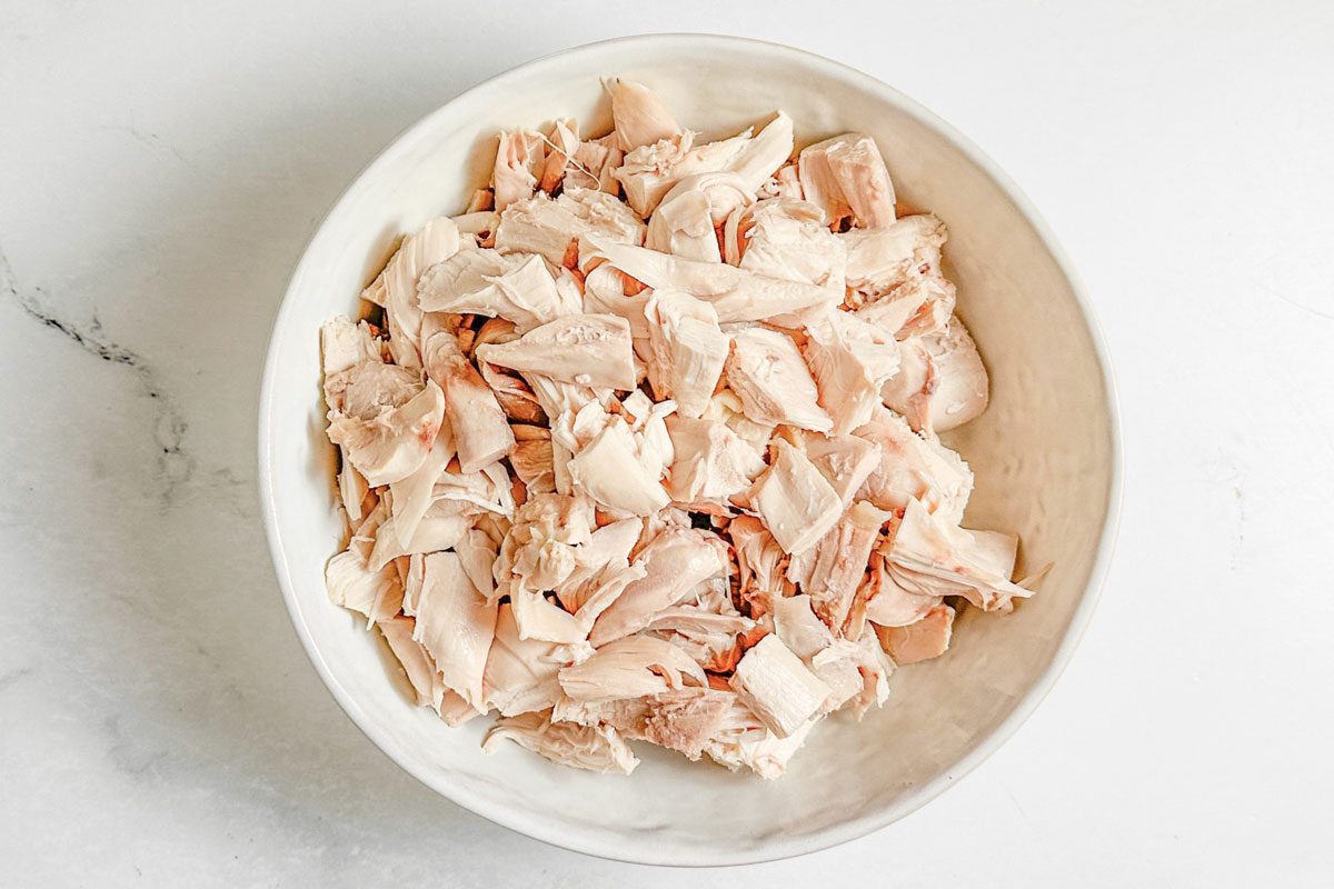 Cooked and shredded chicken in a ceramic bowl for Taste of home Copycat Cracker Barrel Chicken and Dumplings