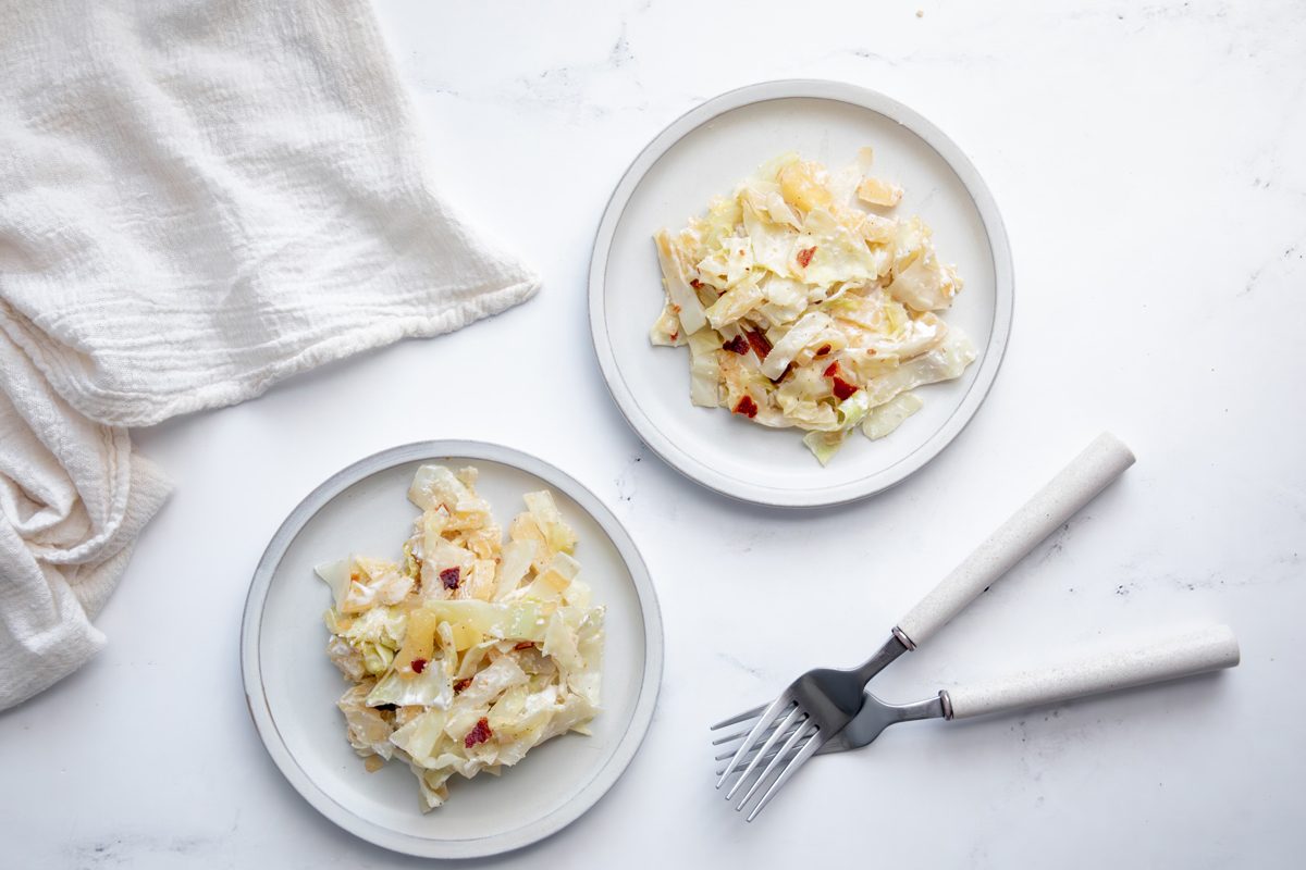 Overhead beauty shot for Taste of Home Creamed Cabbage topped with bacon on a marble surface with linen.