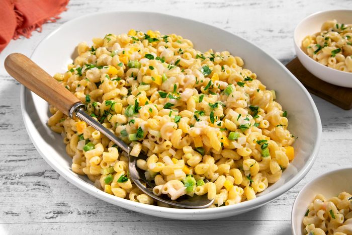 3/4th shot; wooden textured background; Creamy Macaroni Salad in a oval plate with spoon; Creamy Macaroni Salad served in two small bowl