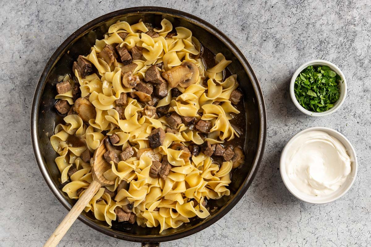 Taste of Home Easy Beef and Noodle recipe photo of the cooked noodles added to the skillet with a side of sour cream and fresh parsley for topping.