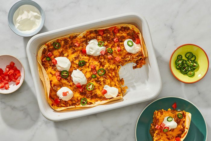 Cooked enchilada casserole with a portion removed and toppings on top