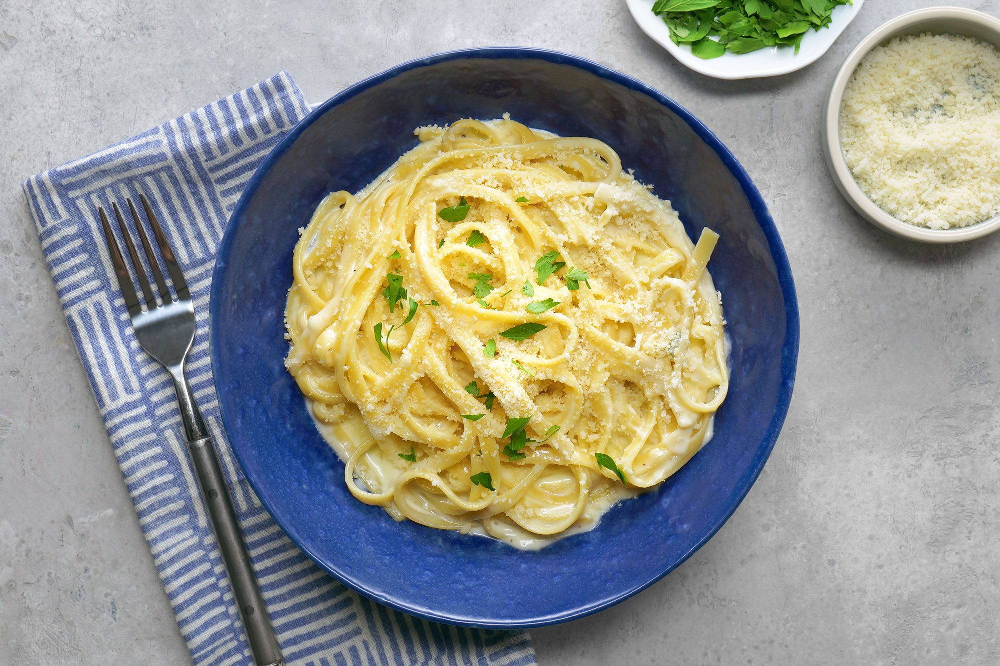 Fettuccine Alfredo pasta is topped with a sprinkle of freshly grated Parmesan cheese and a garnish of chopped parsley