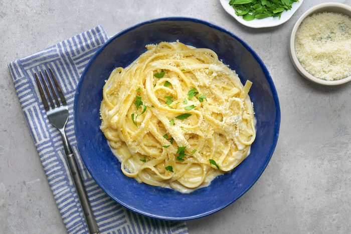 Fettuccine Alfredo pasta is topped with a sprinkle of freshly grated Parmesan cheese and a garnish of chopped parsley